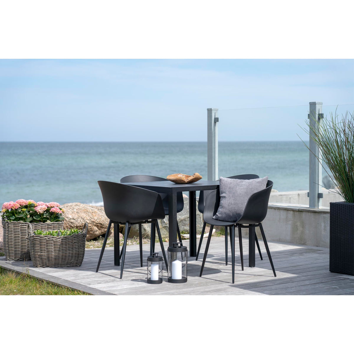 Quatre chaises Roda noires autour d'une table carrée noire sur une terrasse en bois face à la mer
