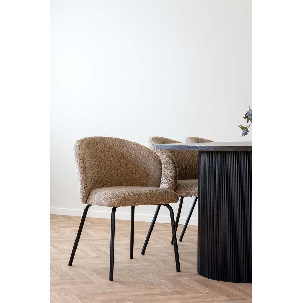 Chaises Safira bouclé beige vues de trois quarts le long d'une table noire à pied cannelé