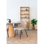 Chaise Safira bouclé beige près d'une table ronde en bois à pied conique devant une bibliothèque