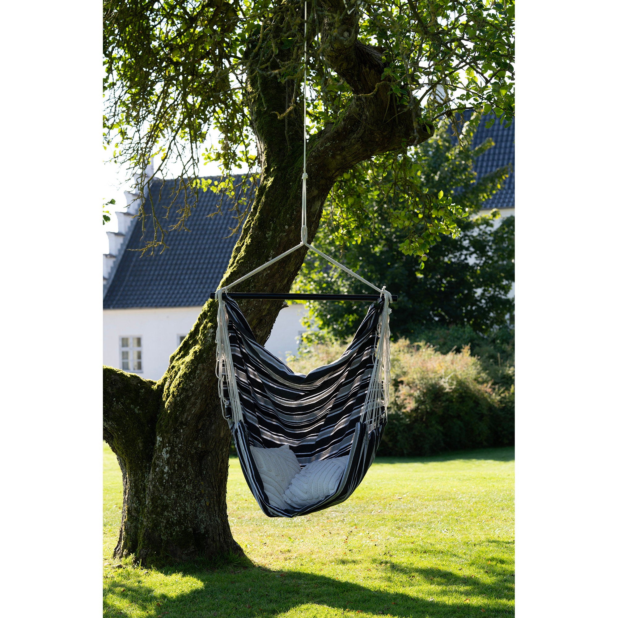 Chaise hamac Lamia rayée noir gris suspendue à un arbre dans un jardin ensoleillé