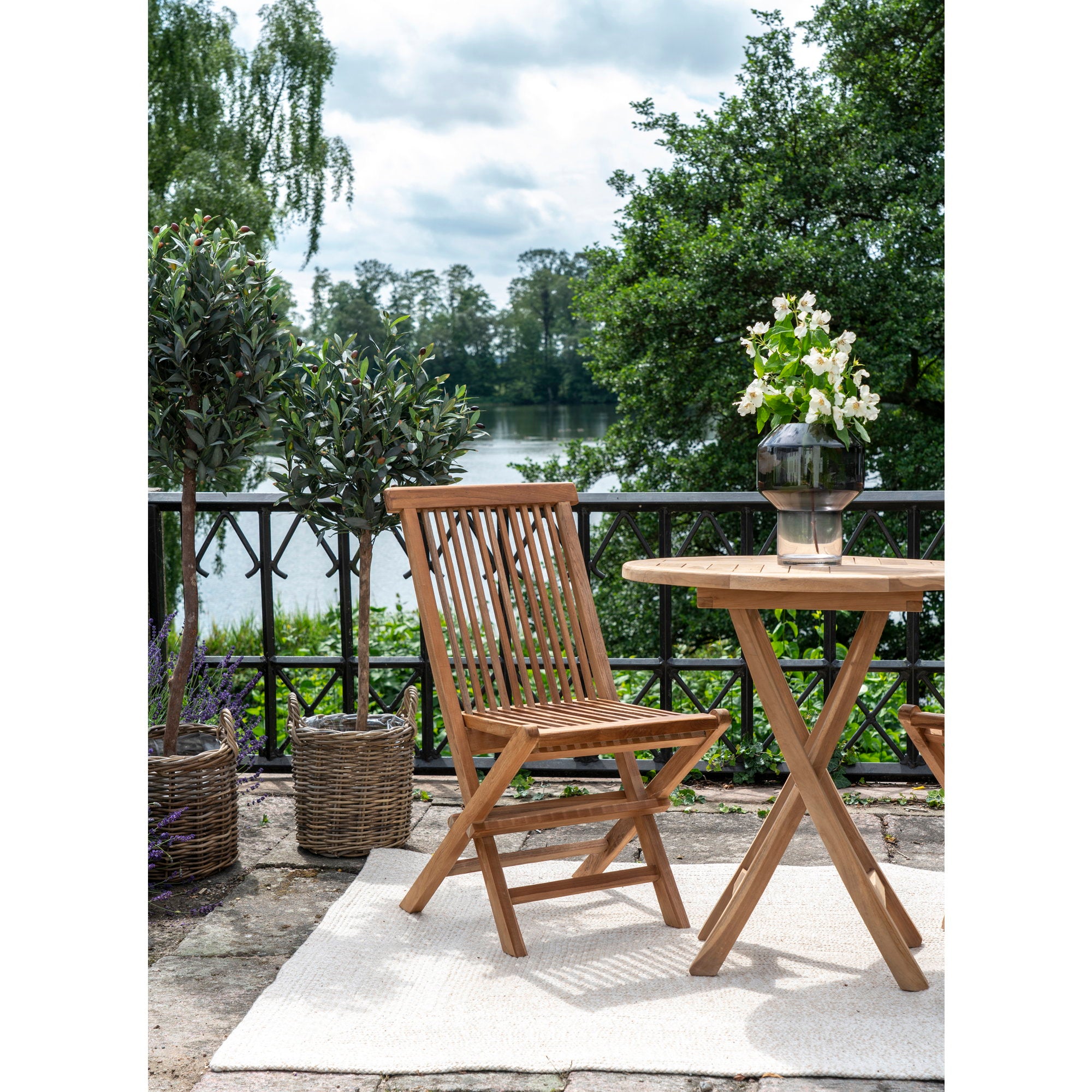 Chaise Toledo teck avec table ronde teck sur terrasse bord de lac avec fleurs blanches