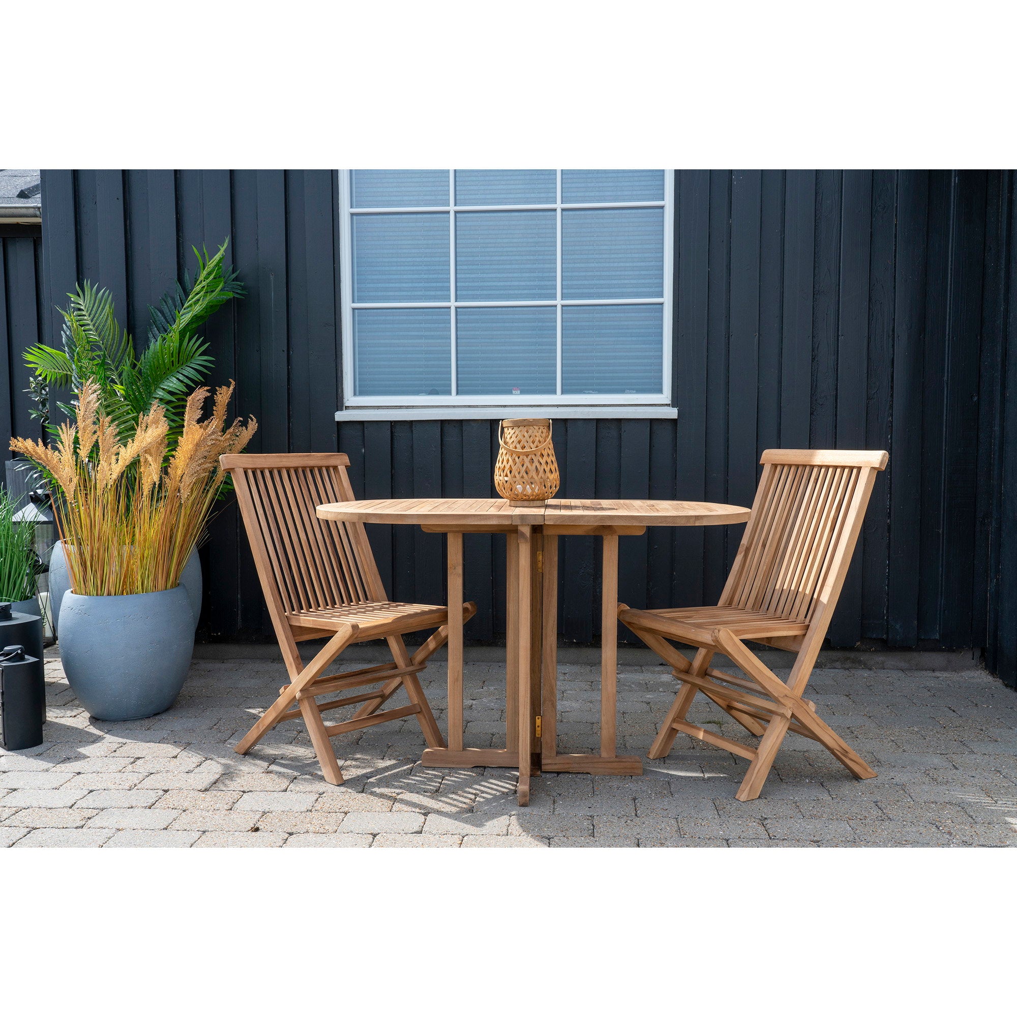 Deux chaises Toledo teck autour table ronde teck, terrasse maison noire et plantes