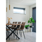 Chaises Middelfart microfibre brun clair alignées autour table bois massif pieds croisés noirs suspensions dorées plantes