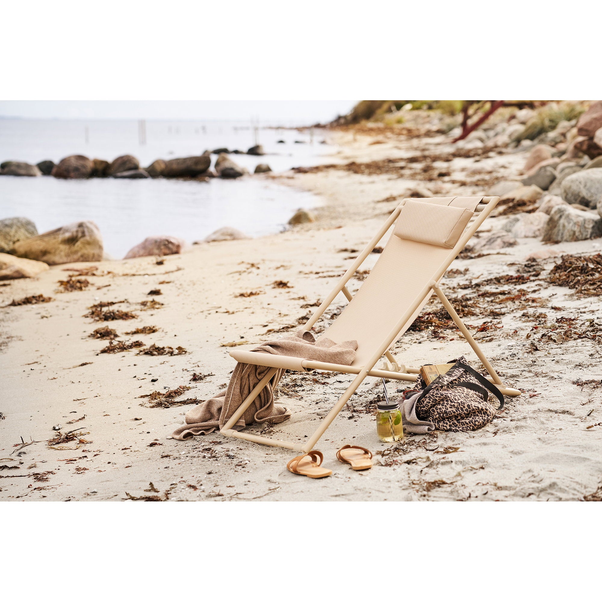 Chaise de plage Curtis taupe posée sur sable face à la mer avec plaid et sac léopard
