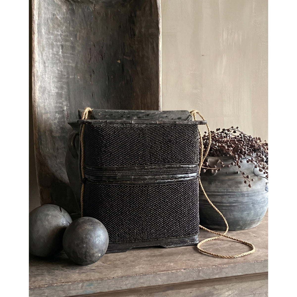 Coffret en perles noires posé sur une console en bois brut entre deux boules patinées et une poterie grise garnie de baies séchées