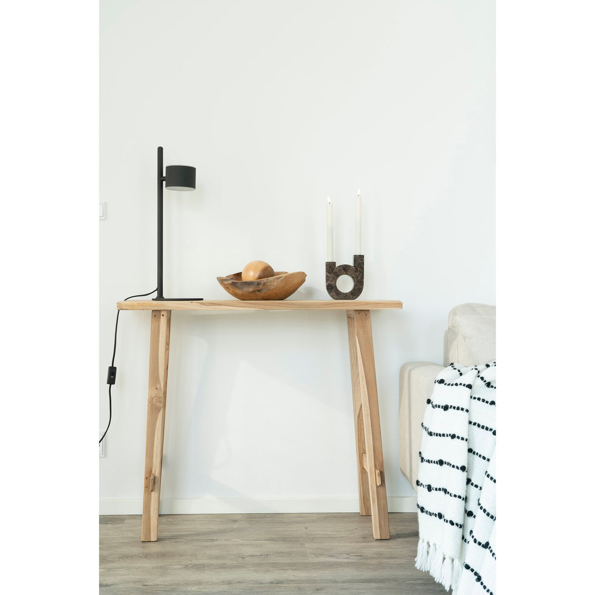 Console Girona en teck avec une lampe noire une coupe en bois et un bougeoir à côté d'un canapé clair