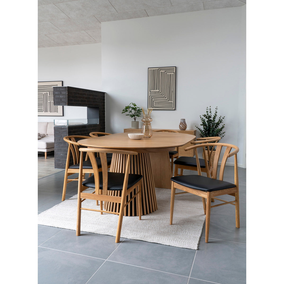 Salle à manger avec la coupe plissée beige posée sur une table ovale en bois à pied à lattes entourée de chaises en bois