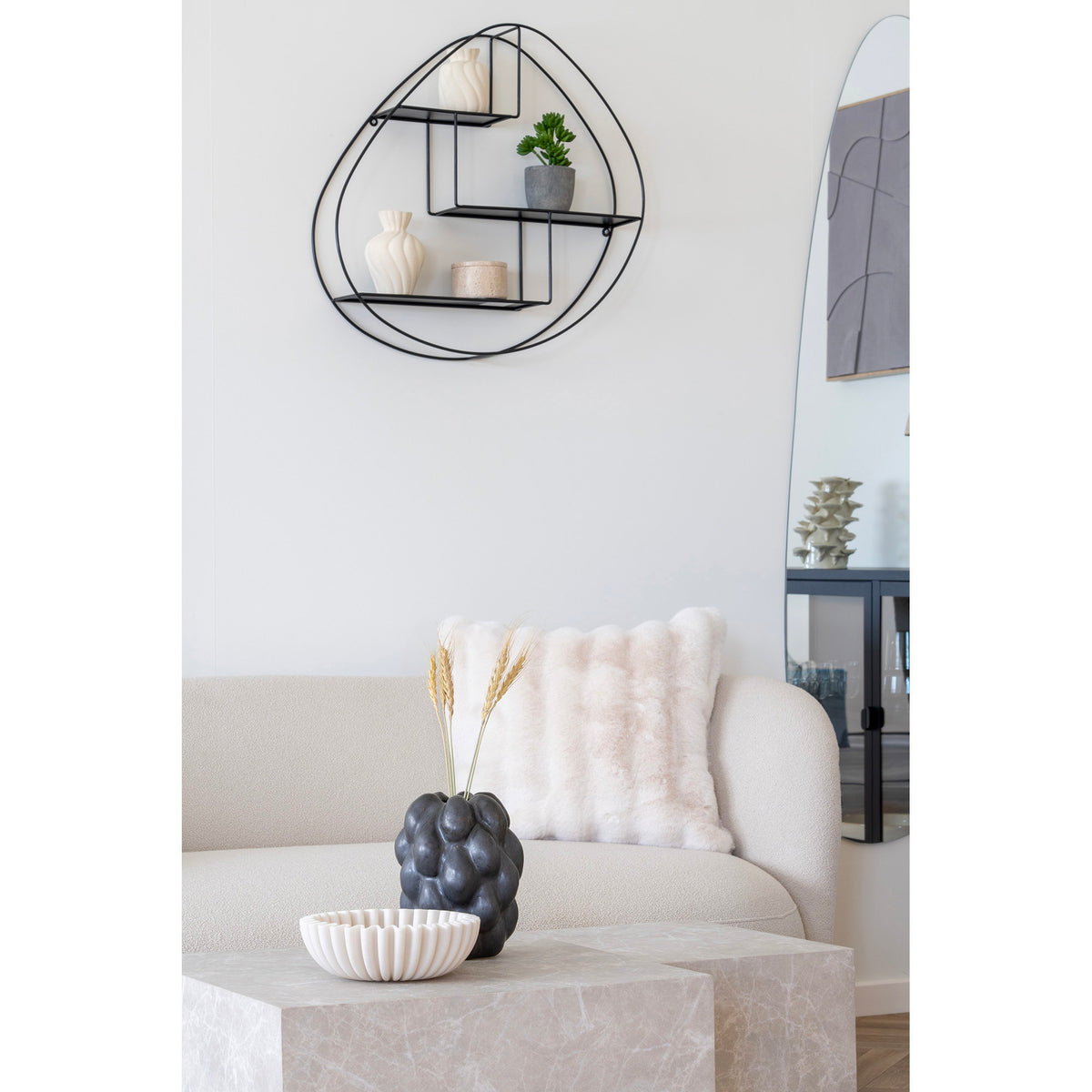 Coupe plissée beige sur une table basse cubique au veinage clair devant un vase sombre garni d'épis de blé et un canapé clair