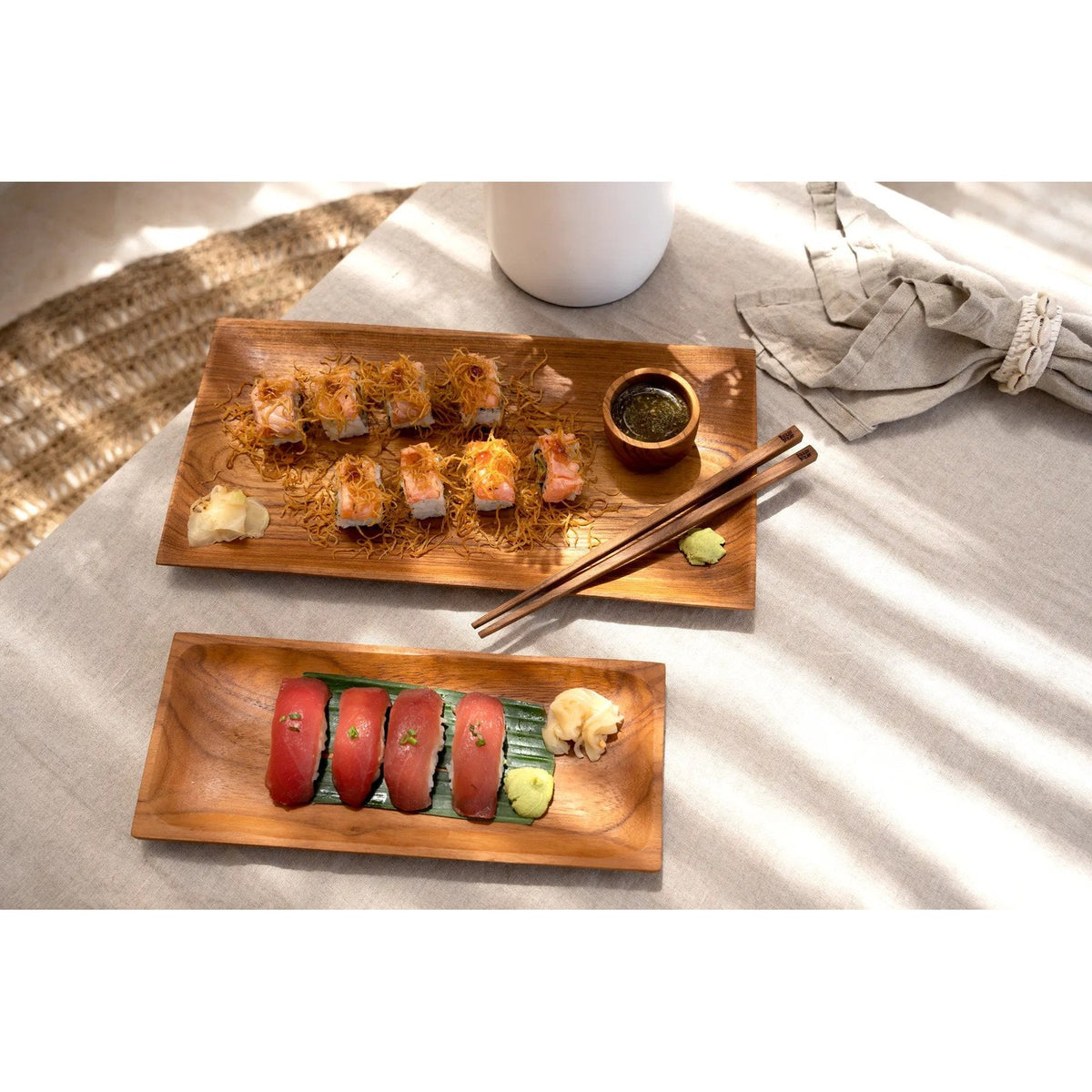 Coupelle en teck remplie de sauce sur un plateau de makis en bois à côté d'un plateau de nigiris et d'une serviette