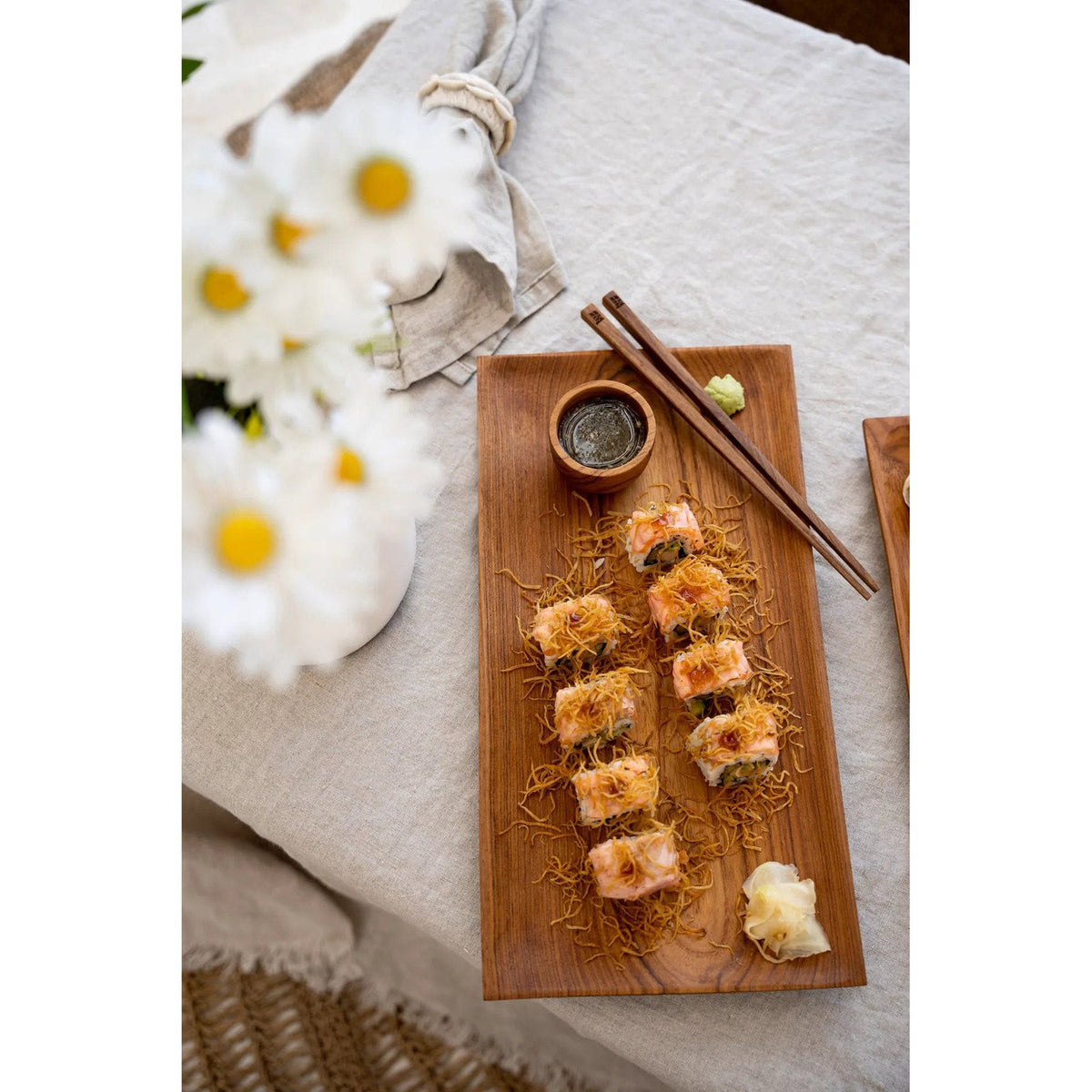 Vue du dessus d'une coupelle en teck remplie de sauce sur un plateau rectangulaire en bois garni de makis avec des baguettes