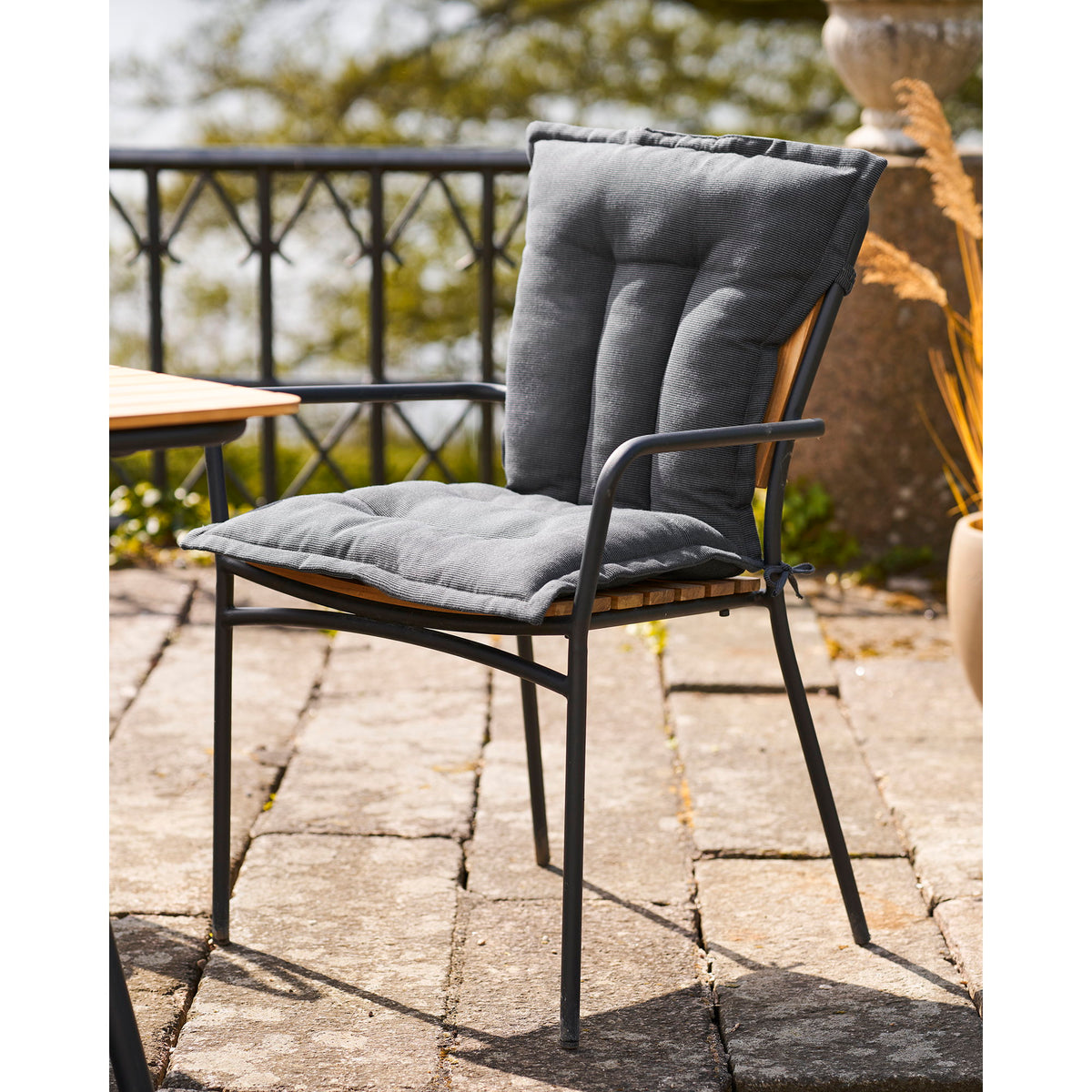 Coussin Cleveland noir sur une chaise de jardin en métal noir et lattes de bois sur une terrasse en pierre
