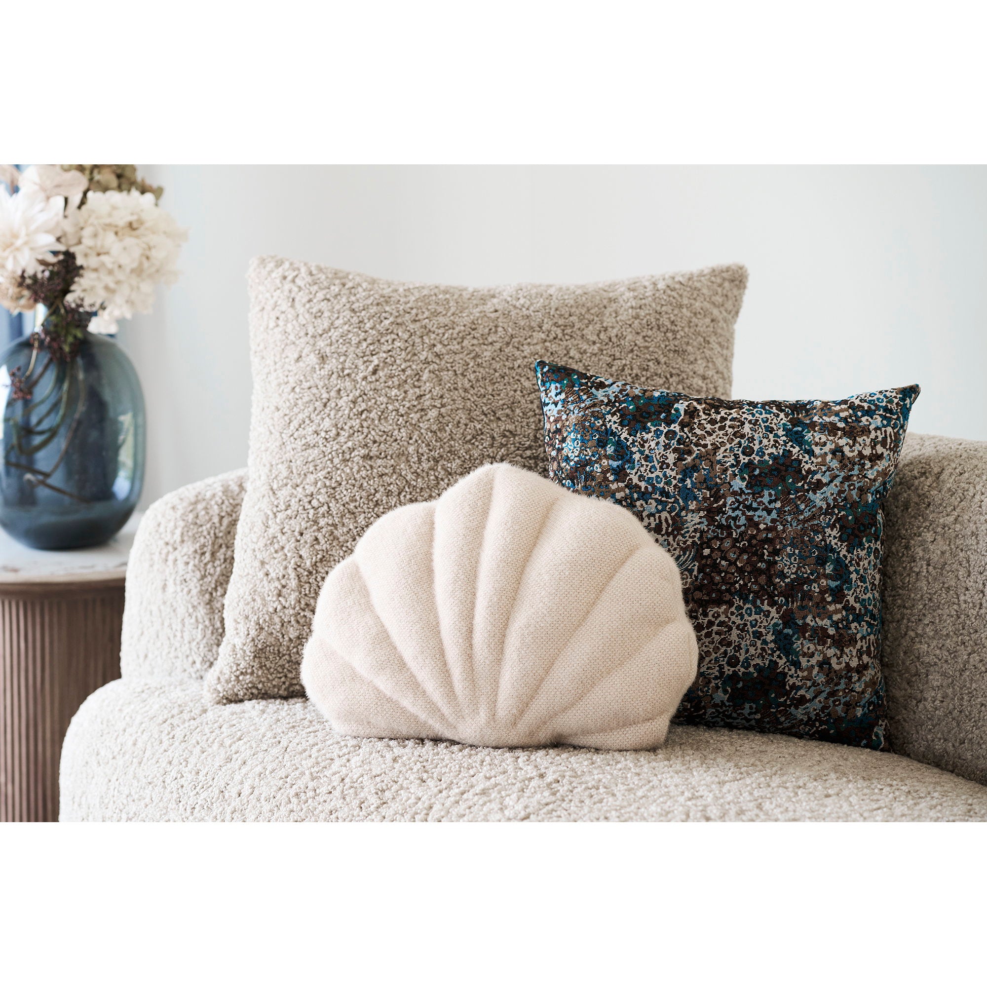 Coussin décoratif Darling coquillage beige posé sur canapé bouclette décor côtier