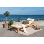 Coussin Andorra blanc sur un bain de soleil en teck sur une terrasse face à la mer avec un plaid et deux lanternes