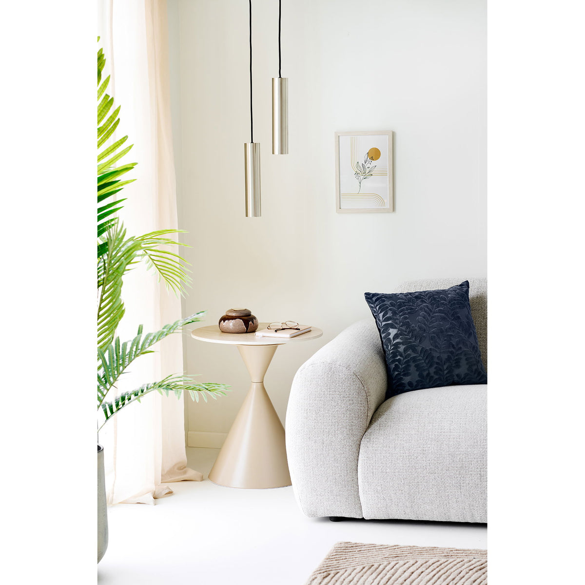 Coussin Yona bleu marine dans l'angle d'un canapé clair près d'un voilage et d'une plante