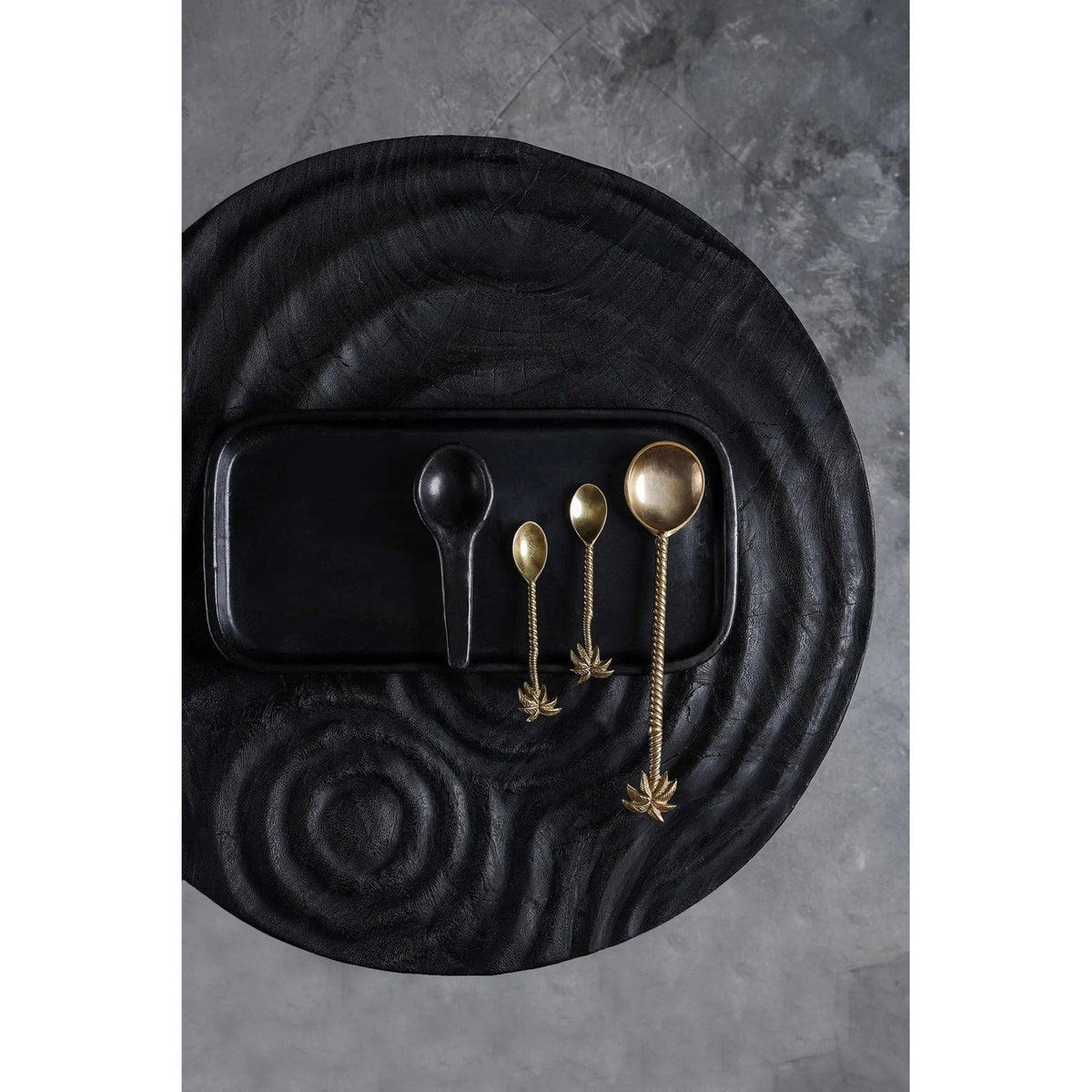 Cuillère à tapas en terre cuite noire sur un plat rectangulaire noir à côté de trois cuillères en laiton à palmier