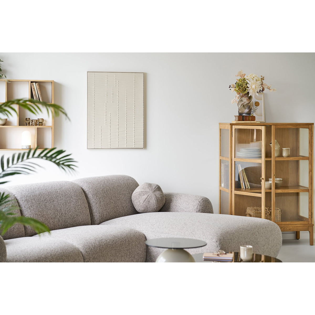 Décoration murale Ena au-dessus d'un canapé gris près d'une vitrine en bois garnie de vaisselle