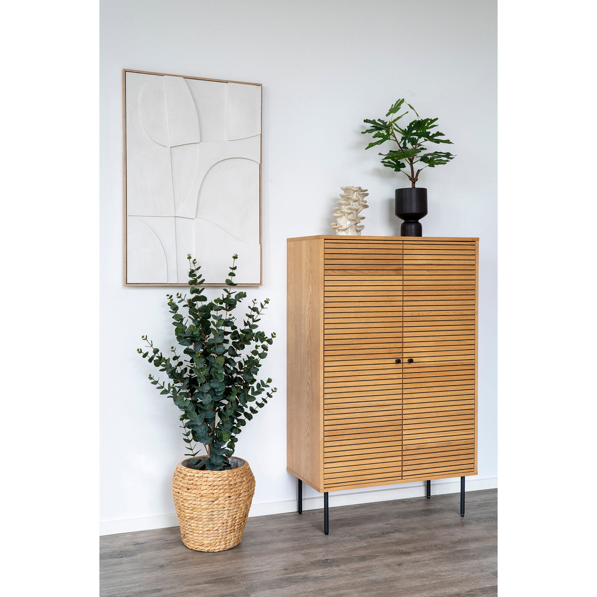 Décoration murale Madeline N°2 blanche accrochée près d'une armoire en bois clair à lamelles et d'un eucalyptus en panier