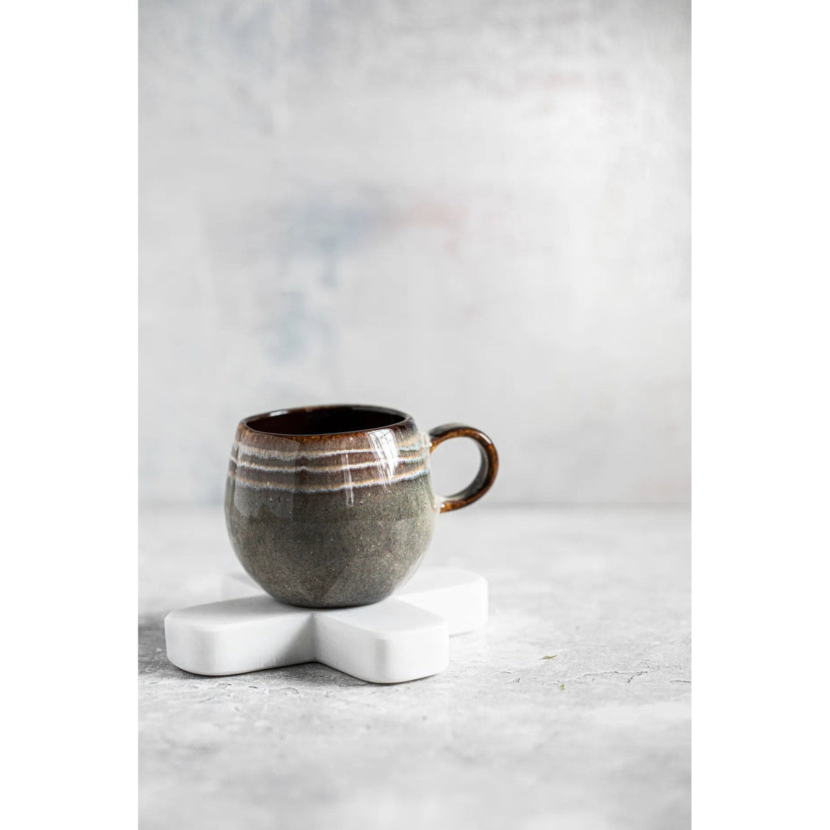 Tasse en grès émaillé posée sur le dessous-de-plat croix en marbre blanc