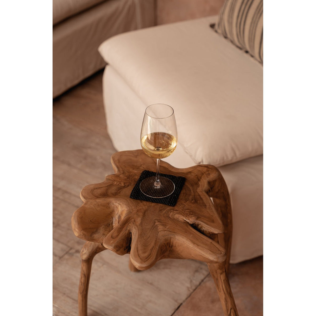 Dessous-de-verre carré en perles noires sous un verre de vin sur une table d'appoint en bois brut devant un canapé clair