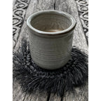Dessous-de-verre en raphia noir sous une tasse en grès gris sur une table en bois sculpté