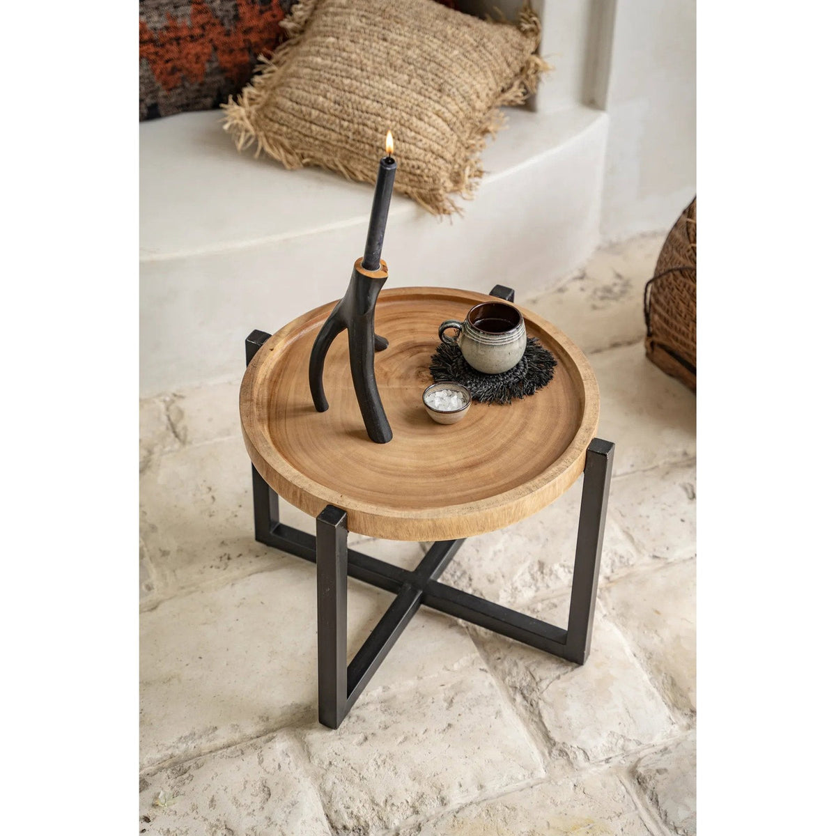 Tasse en grès sur le dessous-de-verre en raphia noir sur une table d'appoint ronde en bois près d'un bougeoir allumé
