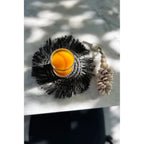 Dessous-de-verre noir à frange sous un verre de jus orangé sur une table en marbre à côté d'un porte-clés en coquillages
