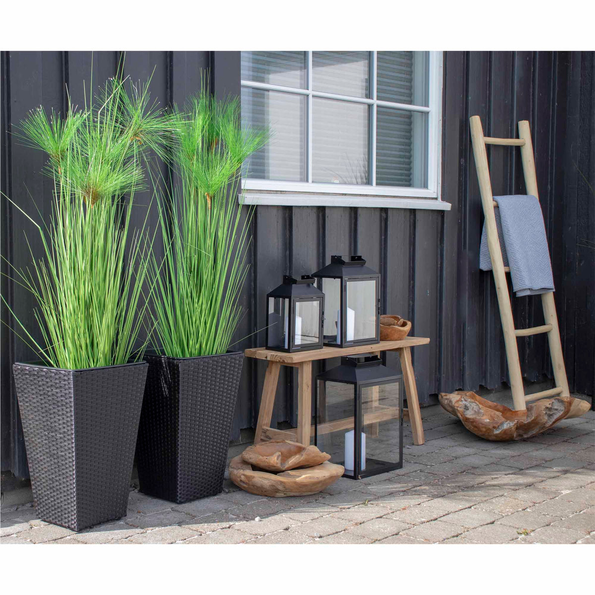 Échelle décorative en teck naturel sur une terrasse avec un plaid gris clair près de lanternes noires
