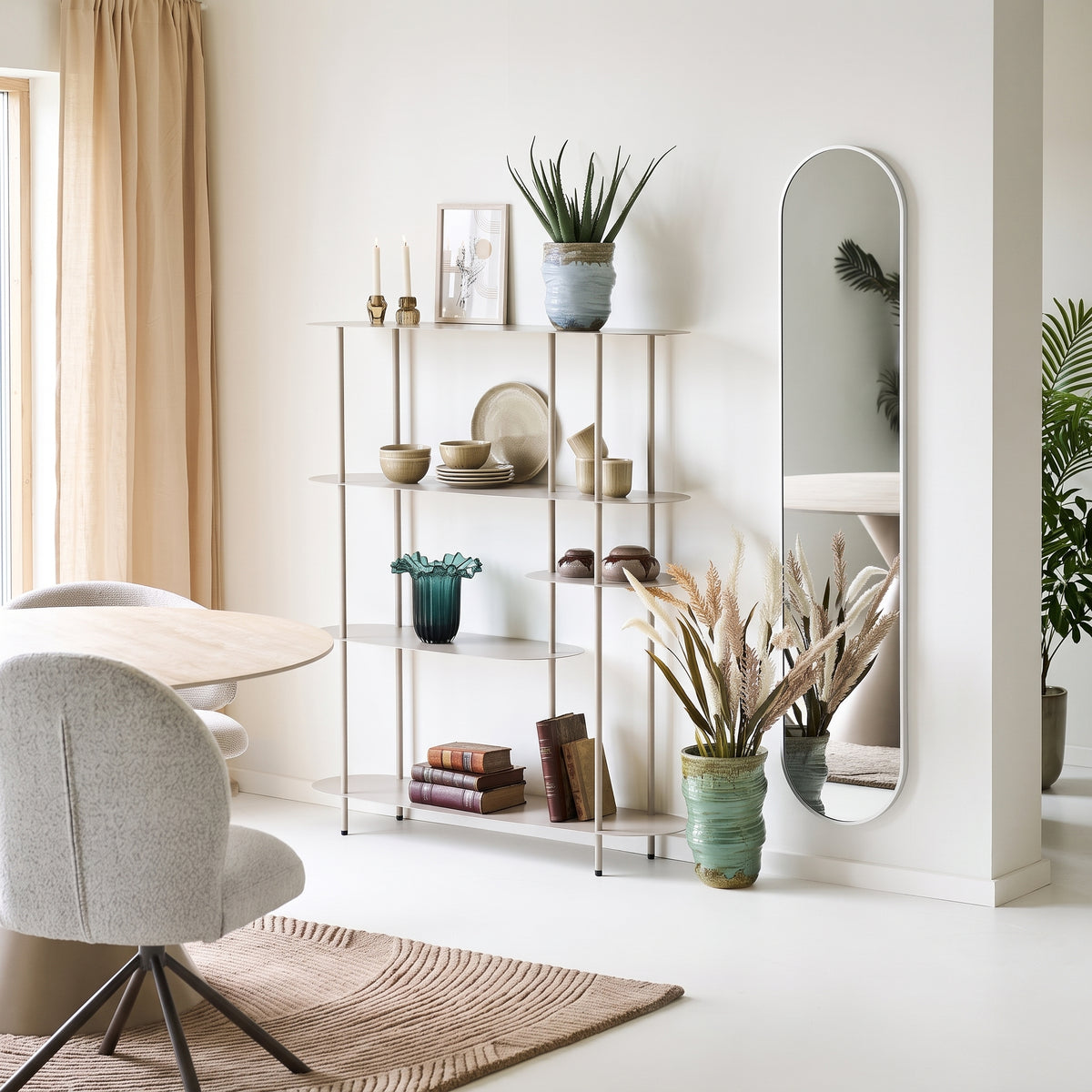 Étagère Rieti asymétrique sable garnie de vaisselle en grès, de livres, de vases et d'un aloès, près d'un miroir ovale et d'une table ronde