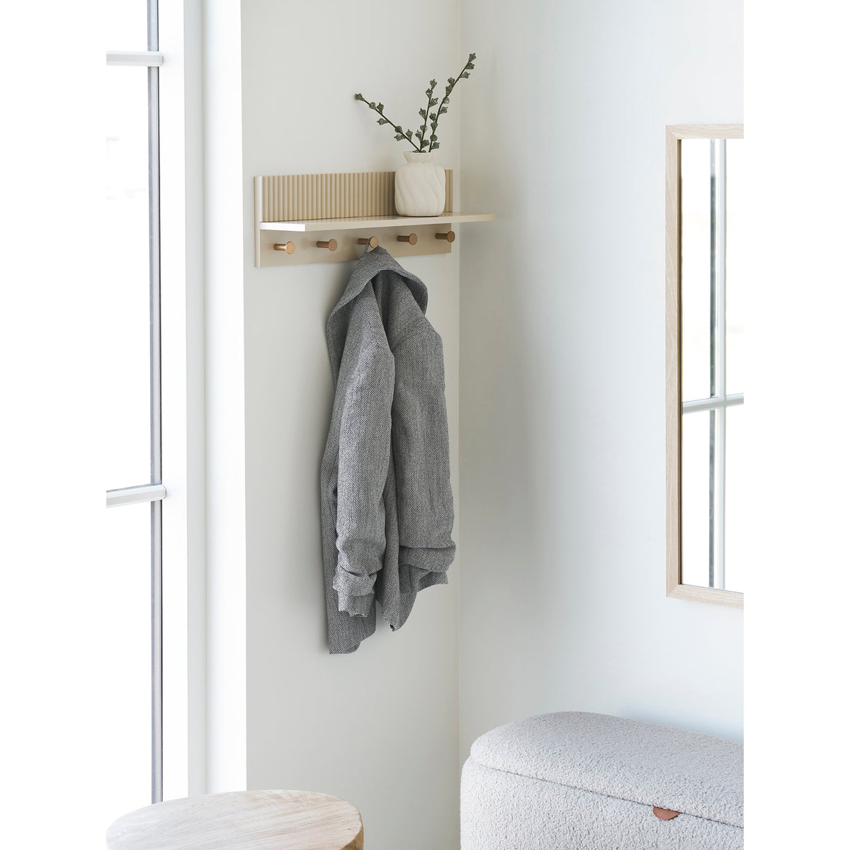 Étagère Rocca beige fixée au mur d'une entrée avec une veste grise suspendue et un petit vase blanc sur la tablette