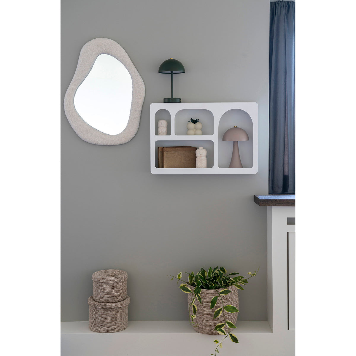 Étagère murale Bryne blanche sur un mur gris garnie de lampes champignon et de figurines près d'un miroir organique