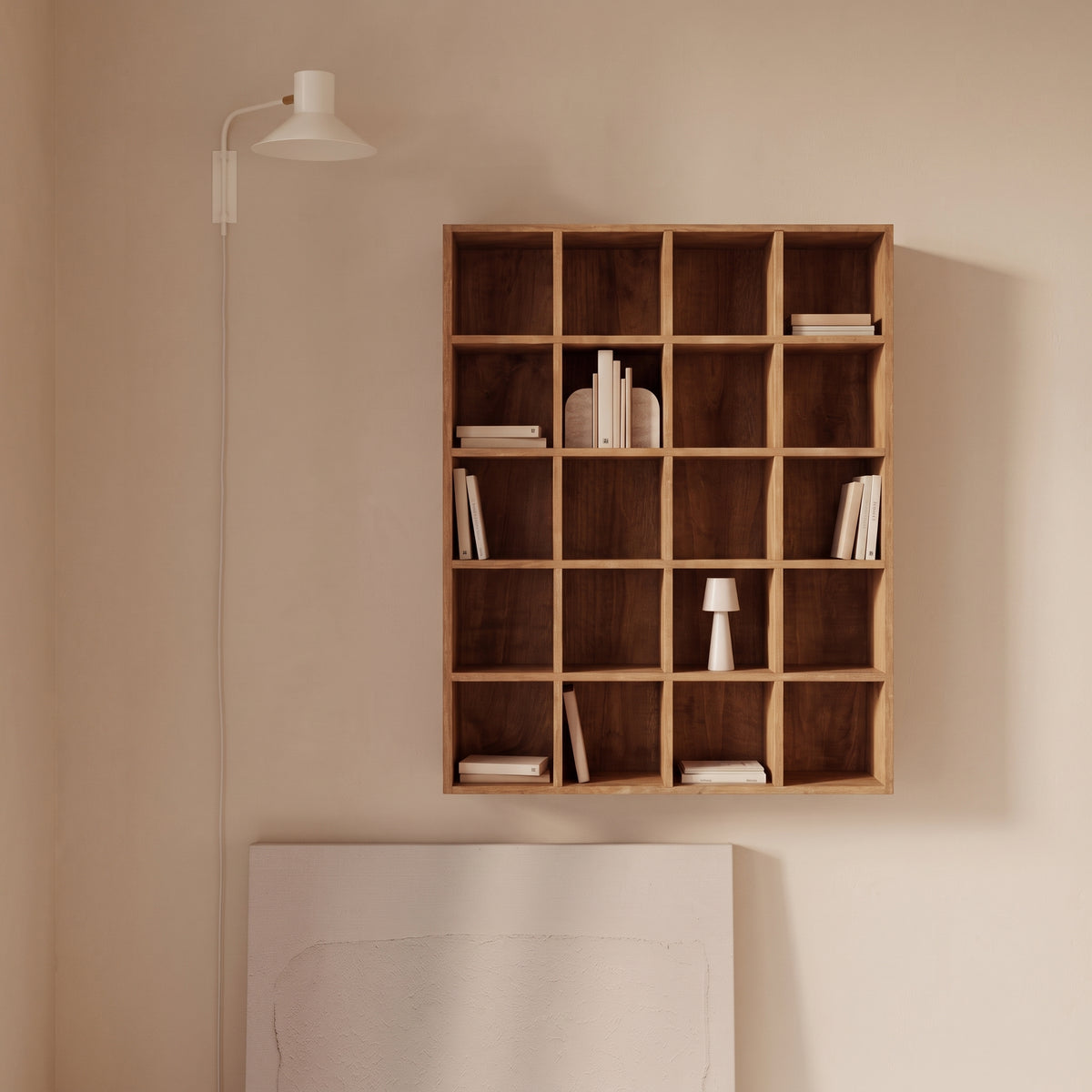 Étagère murale Moss en pin naturel accrochée au-dessus d'un tableau, quelques livres et une lampe dans ses cases, à côté d'une applique blanche