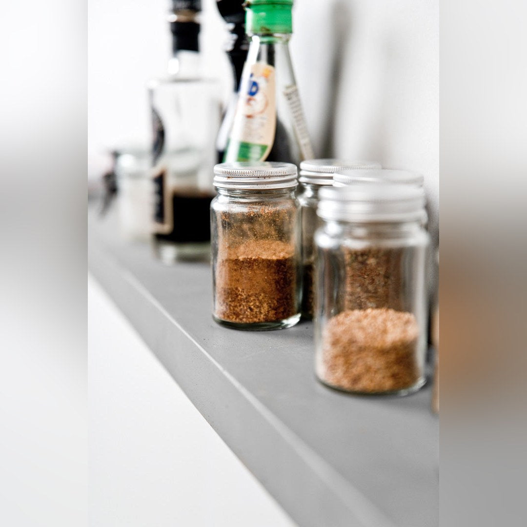 Étagère murale Sliced en béton gris vue de près avec des bocaux d'épices en verre et des bouteilles