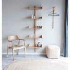 Étagère murale Villa en bambou fixée sur un mur gris clair entre une chaise en bois à assise tressée et un pouf écru