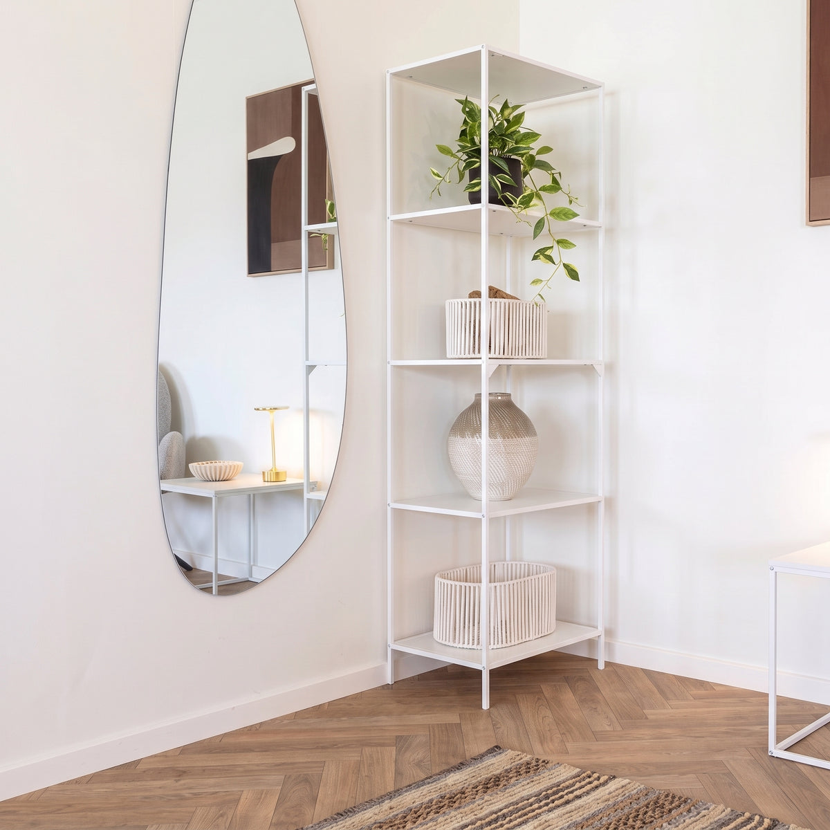 Étagère Vita en acier blanc garnie d'une plante retombante, de paniers et d'un vase, à côté d'un grand miroir