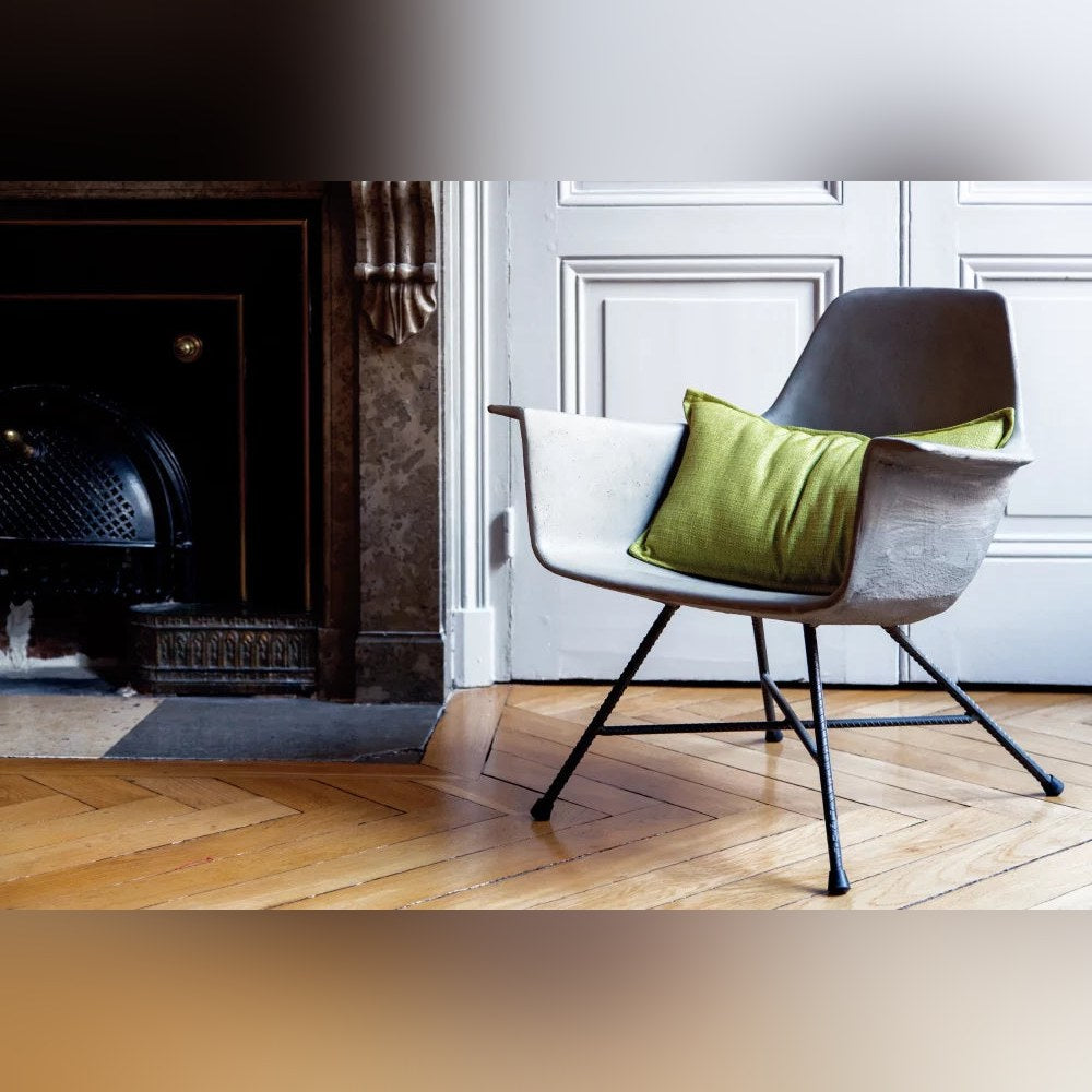 Fauteuil bas Hauteville avec un coussin vert près d'une cheminée en marbre sur un parquet en bois clair
