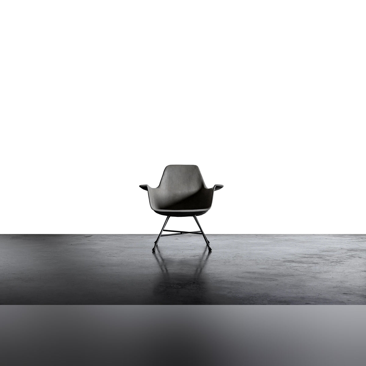 Fauteuil bas Hauteville vu de face sur un sol en béton lissé devant un fond blanc