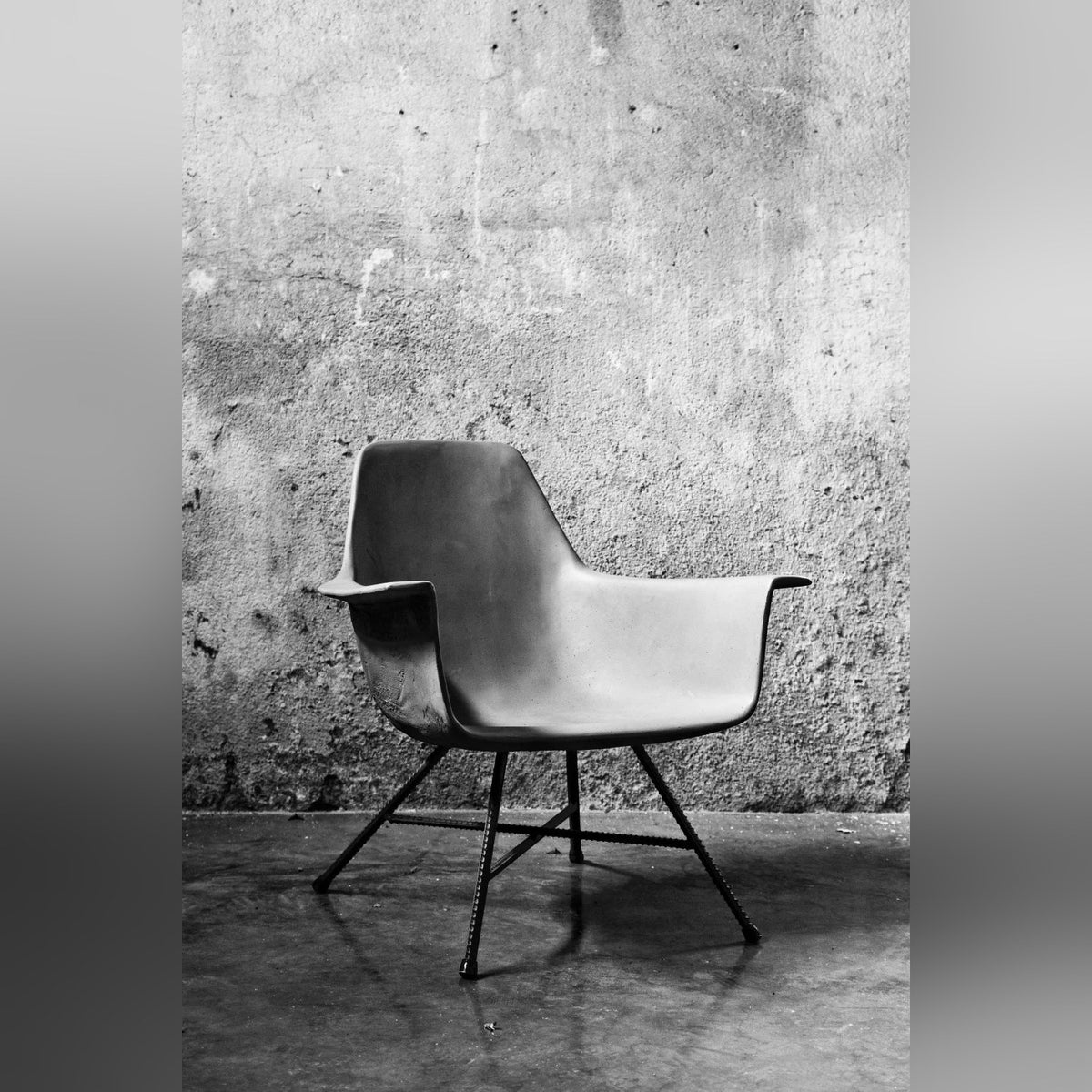 Fauteuil bas Hauteville de trois quarts devant un mur en béton brut en noir et blanc
