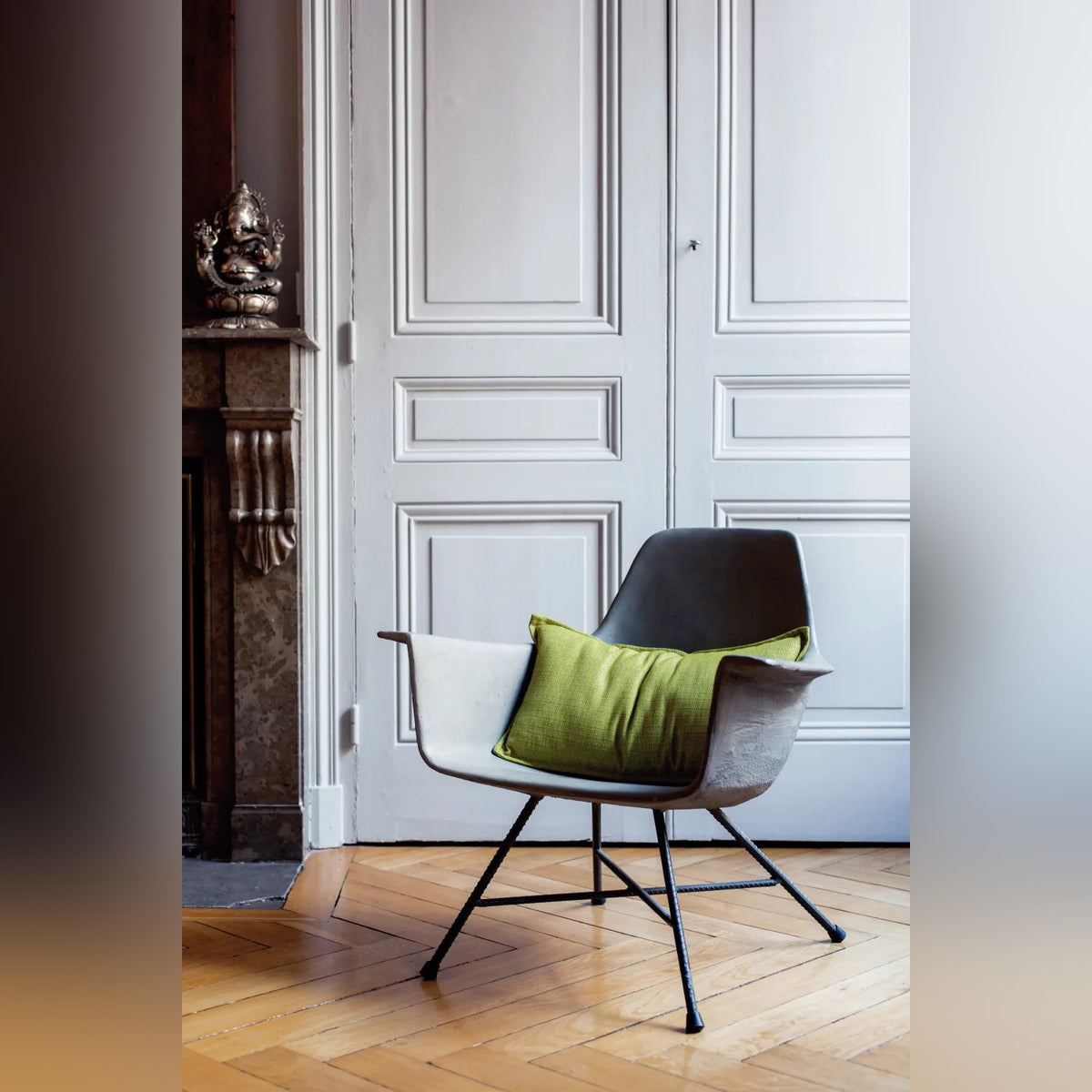 Fauteuil bas Hauteville gris naturel avec un coussin vert devant des portes moulurées sur un parquet en bois clair