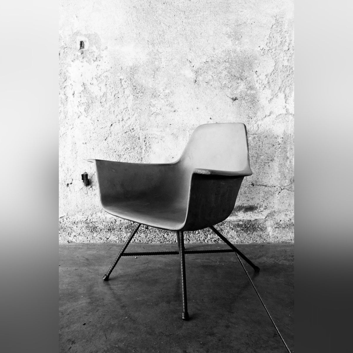 Fauteuil bas Hauteville vu de profil devant un mur en béton brut en noir et blanc