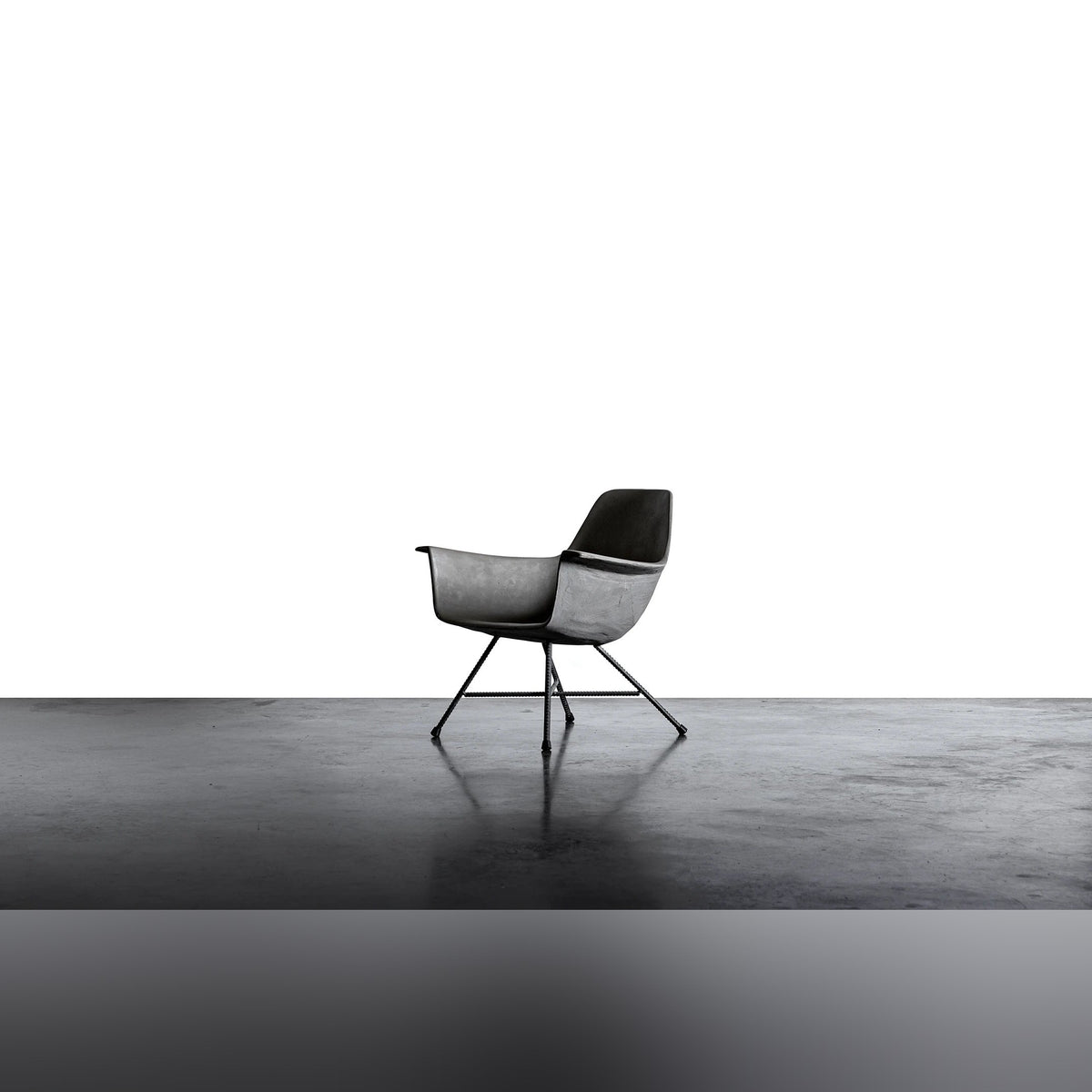 Fauteuil bas Hauteville vu de trois quarts sur un sol en béton lissé