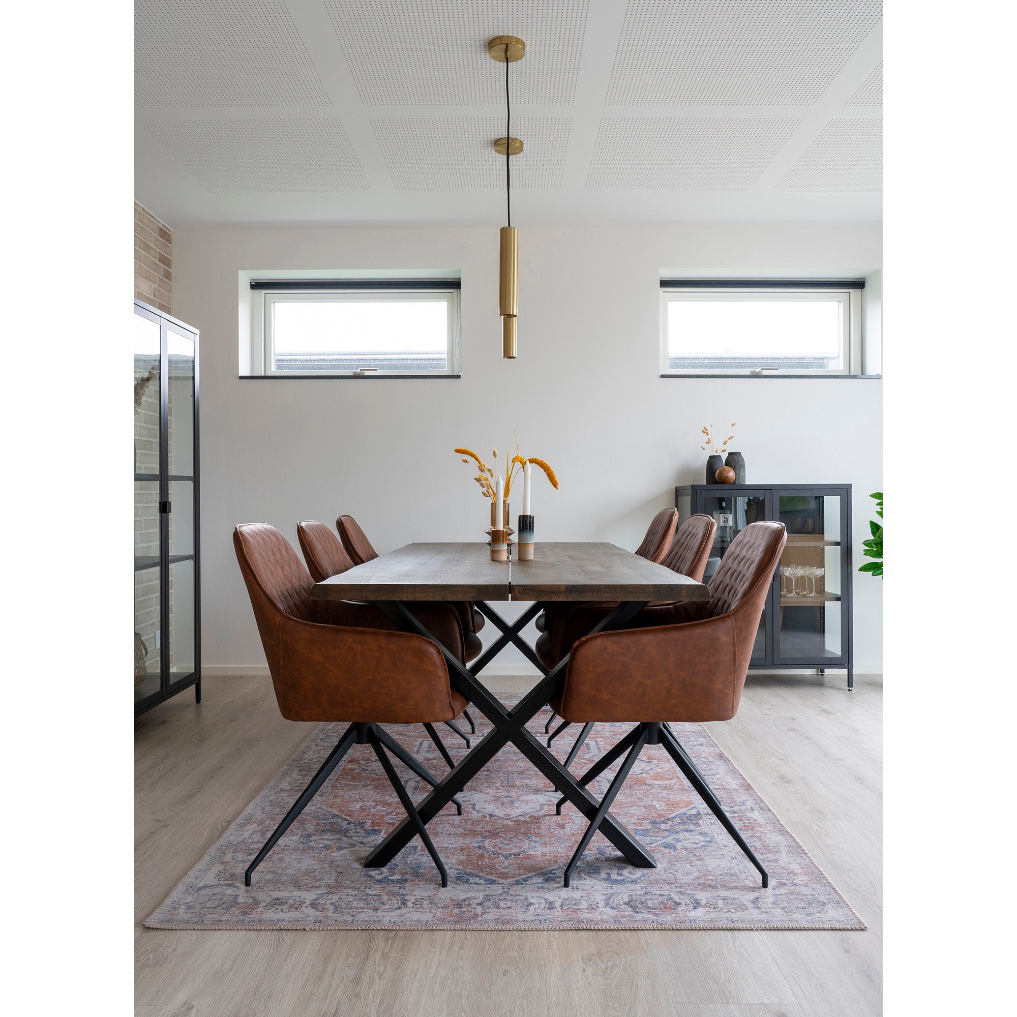 Fauteuils Harbo pivotants cuir vintage brun autour table bois massif pieds croisés avec vitrine noire et suspensions dorées