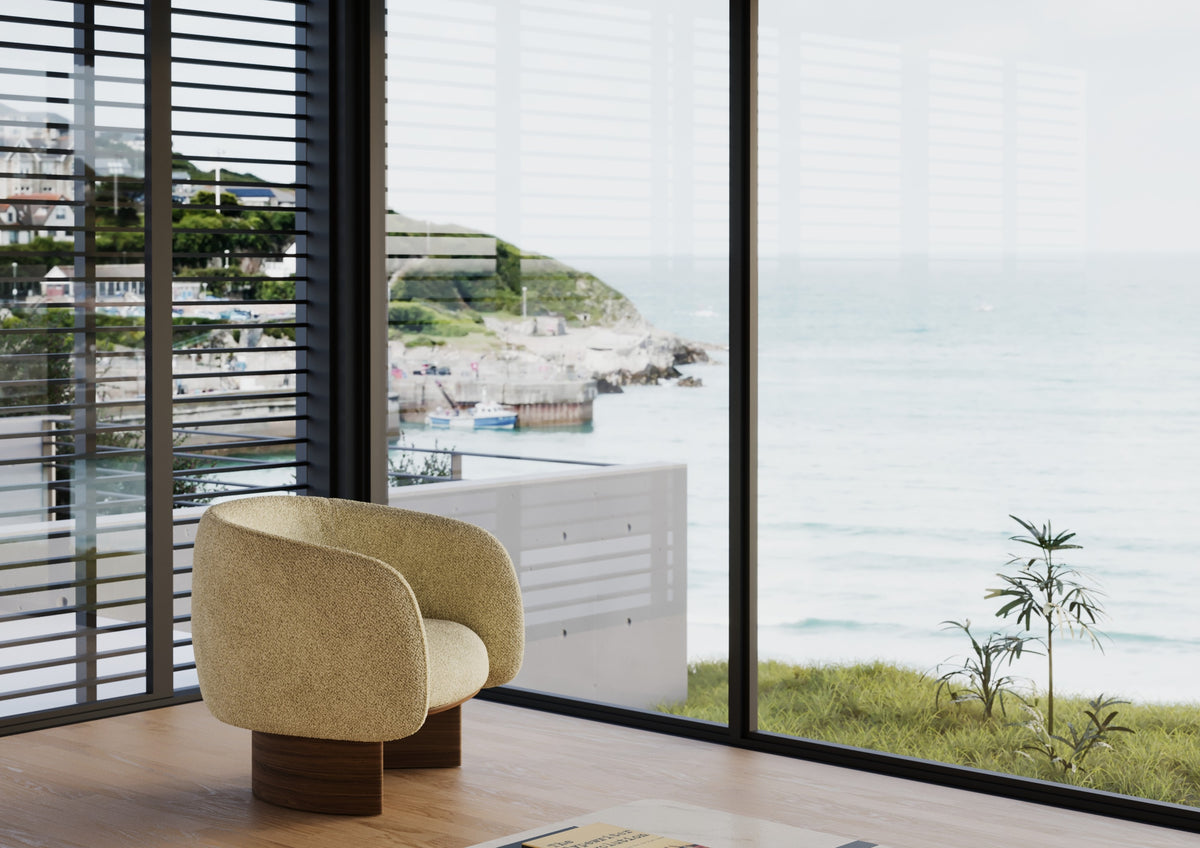 Fauteuil lounge Nido en tissu sable devant une baie vitrée sur la mer