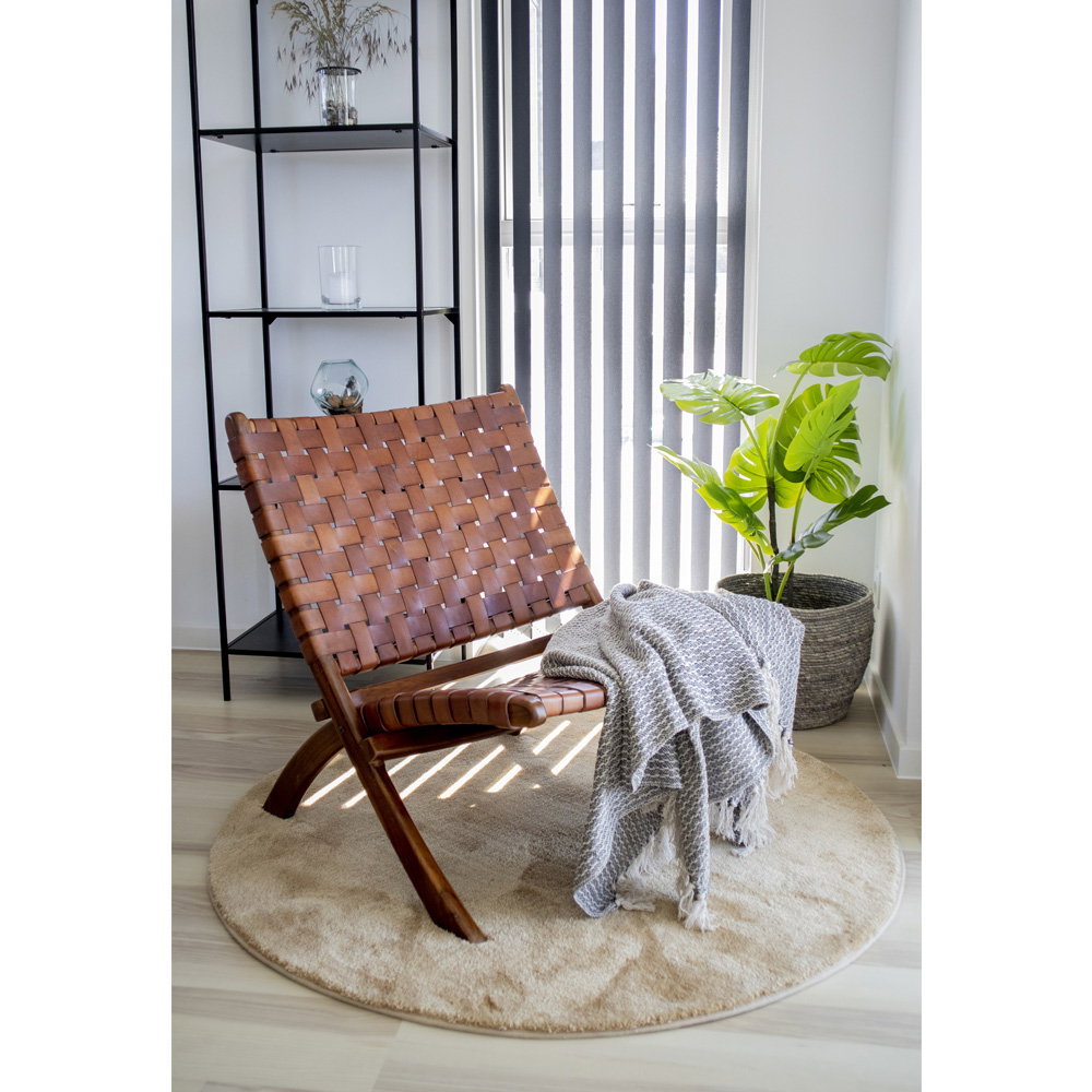 Fauteuil Perugia cuir tressé cognac dans un coin lecture lumineux avec tapis rond et plante tropicale