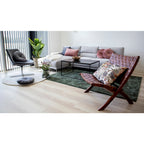 Fauteuil pliant Perugia cuir tressé cognac dans un salon contemporain avec canapé gris et tapis vert
