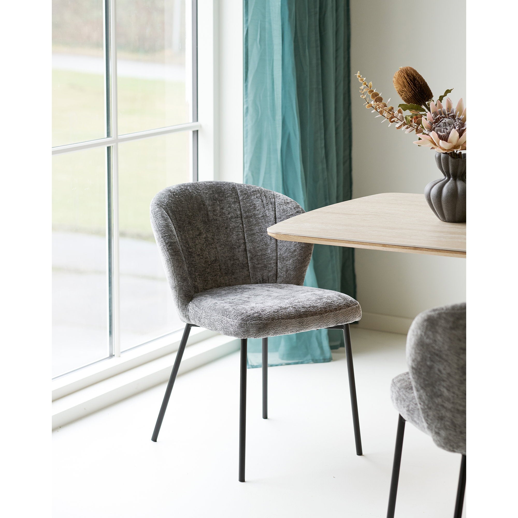 Fauteuil Roanne chenille gris posé près d'une table en chêne dans un espace repas lumineux contemporain