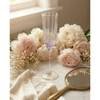 Flûte à champagne irisée lilas sur une table en marbre entourée de pivoines près d'un miroir à main doré