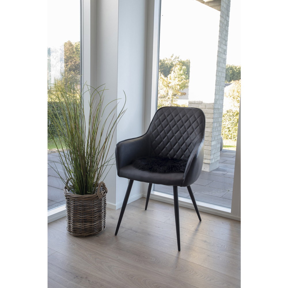 Galette ronde fausse fourrure noir posée fauteuil cuir noir salon lumineux parquet