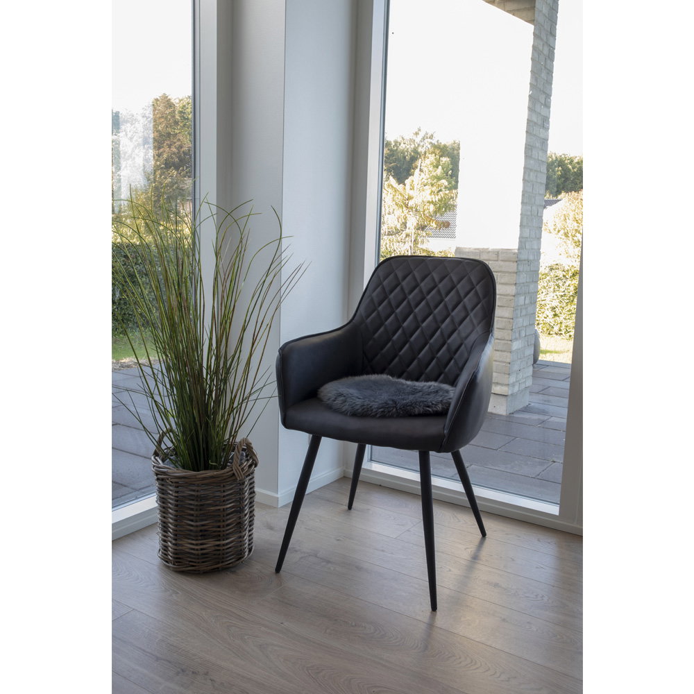 Galette vraie peau d'agneau grise posée sur fauteuil noir capitonné ambiance scandinave lumineuse