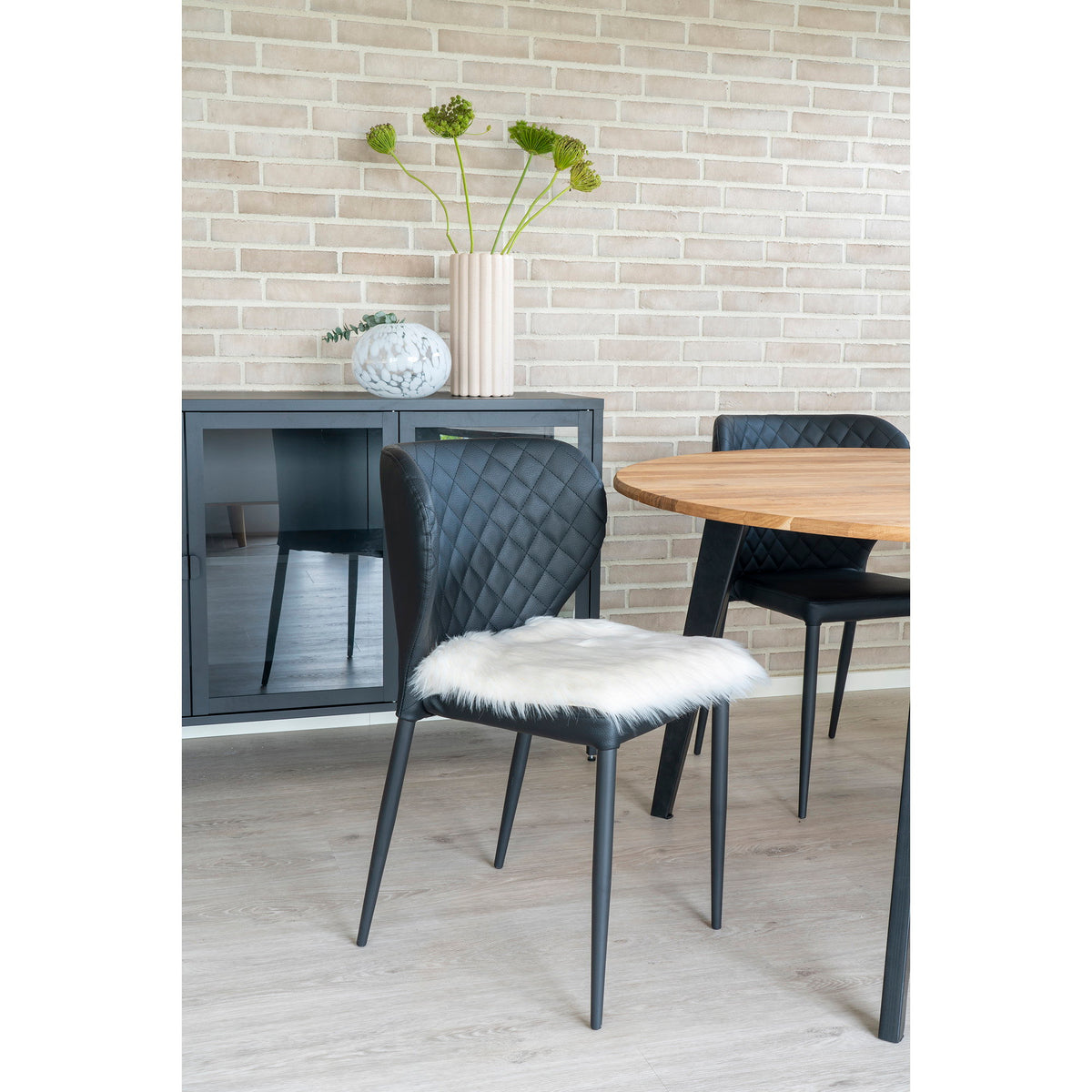 Galette en fausse fourrure blanc ivoire posée sur une chaise noire matelassée près d'une table ronde en bois