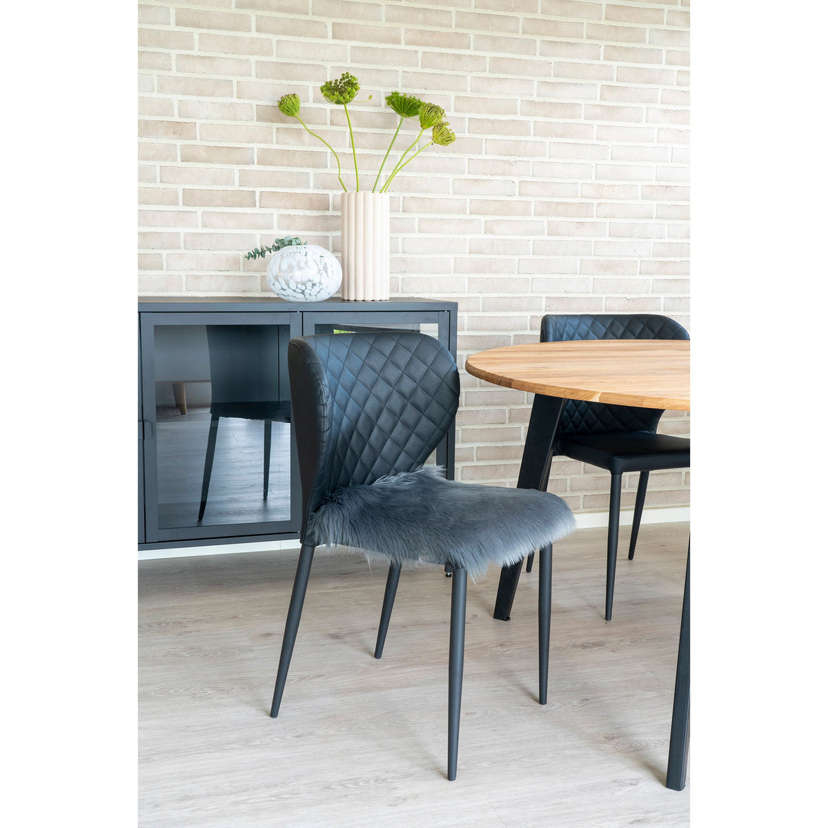 Galette en fausse fourrure grise posée sur une chaise noire matelassée près d'une table ronde en bois
